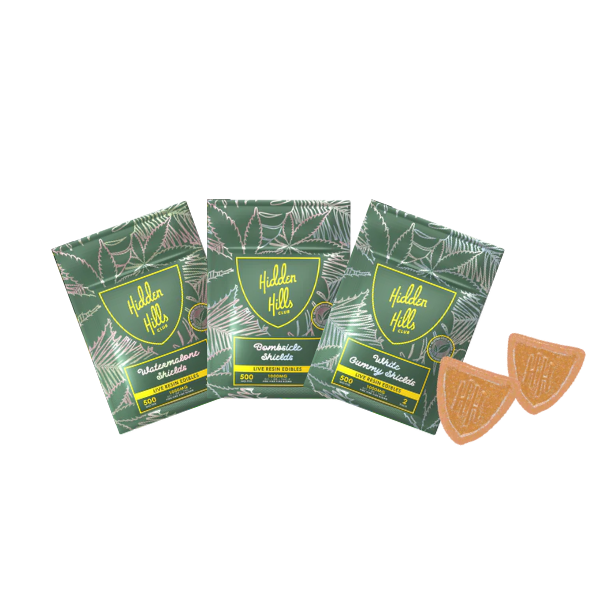 Three green Hidden Hills Shield Gummies | 2ct packages with flavors: Watermelon Hibiscus, Dramatic Black Hole, and Space Orange Nebula—now enriched with Delta 9. Two semi-circle gummies are to the right of the packages.