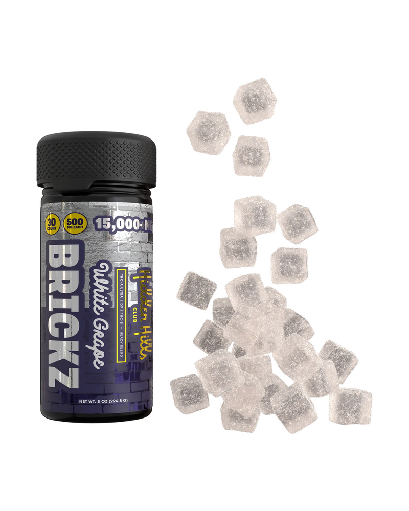 A container labeled "Hidden Hills Heady Blend Brickz Gummies | 15000mg," containing 15,000 mg of Delta 8 THC and live resin, is next to several gummy cubes scattered on a white surface.