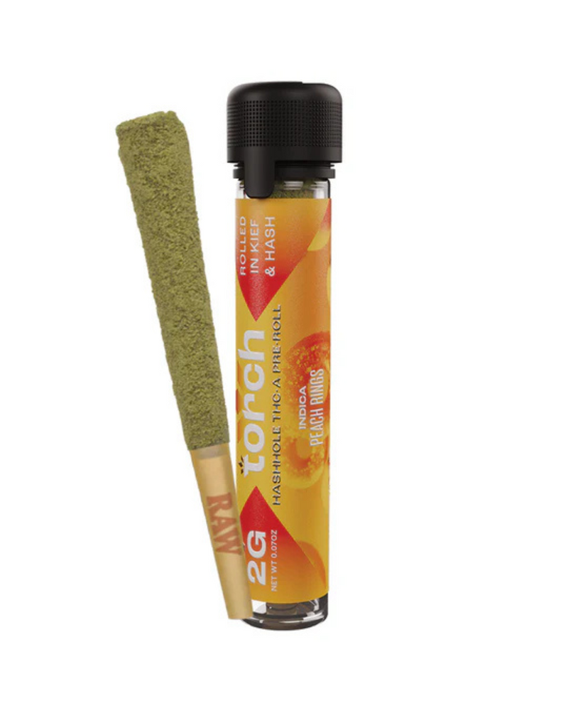 A Torch Hashhole THCA Pre-Roll, infused with hash and coated in green, stands upright beside a transparent tube labeled "Torch" and "Peach Ringz.